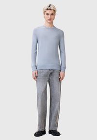 Maglione azzurro chiaro a maglia con scollo rotondo e maniche lunghe, abbinato a jeans grigi a gamba larga strappati e scarpe nere.