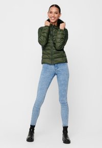 Grønn puffjakke med hette, glidelås og quiltet tekstur. Brukt over lyseblå jeans og svarte ankelstøvler.