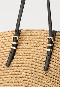 Geweven stro draagtas in natuurlijke kleur met zwarte leren bandjes. Heeft hardware in goudkleur en een kenmerkende sluiting.