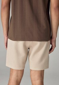 Brun, struktureret top med lodrette striber, parret med beige, vævede shorts med et subtilt mønster og lige kant.