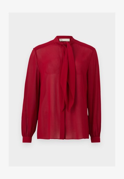 Blouse rouge transparente à manches longues avec un nœud à nouer au col et des poignets à boutons, présentée sur un fond clair uni.