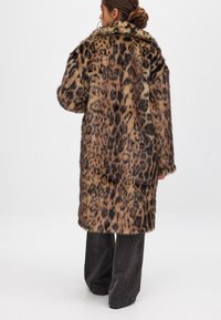 Leopardenmuster Kunstfellmantel mit weicher Textur, langen Ärmeln und breitem Kragen, kombiniert mit dunklen Cordhosen.
