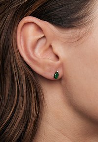 Zielona kamienna kolczyk w kształcie owalu, osadzony w metalu z małym akcentem, prezentowany na ludzkim uchu.