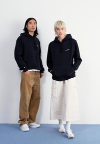 Tumed kapuutsiga jakid ees oleva taskuga, heledad korduroypüksid ja pikk valge seelik. Jalatsiteks on valged tennisetossud helesiniste detailidega.