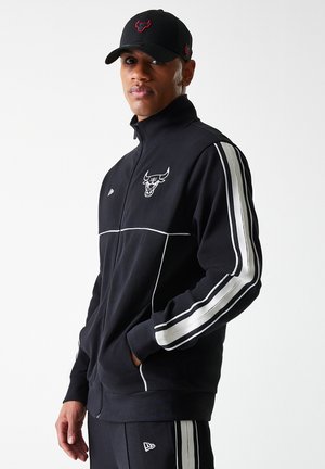 Black zip-up athletic jacket with white stripes along sleeves, featuring a logo on the chest. Material appears textured and sporty.