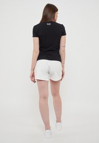 T-shirt nera a maniche corte con un piccolo logo EA7 sul retro, abbinata a pantaloni corti bianchi. Tessuto liscio, design semplice e colori neutri.