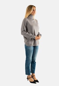 Suéter de cuello alto gris con mangas largas, complementado con jeans de mezclilla azul claro y tacones negros de punta. Textura suave, fit casual.