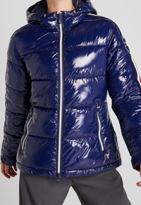 Giacca puffer blu navy con finitura lucida, caratterizzata da una chiusura frontale con zip, cappuccio e strisce laterali a contrasto. Design trapuntato texture.