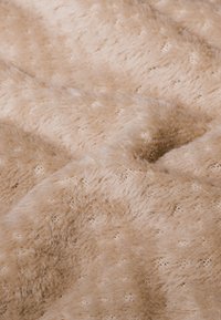 Tissu en velours beige avec une surface douce et texturée, présentant un motif subtil et un léger éclat, créant une apparence chaleureuse et confortable.