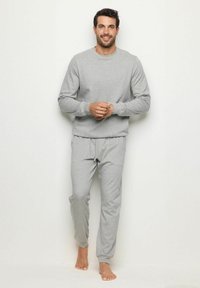 Hanorac gri deschis și pereche de pantaloni joggeri asortați, made dintr-un material moale. Hanoracul are mâneci lungi și un decolteu rotund.