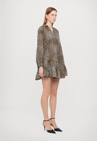 Haljina s uzorkom leoparda, s ovratnikom, dugim rukavima i nabranim rubom. Izrađena od lagane tkanine, ima kroj koji naglašava figuru.