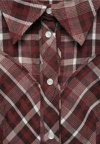 Košile v burgundské a bílé kostkované vzoru s límečkem a stříbrnými patentkami vpředu, s viditelnou texturou látky v provedení.