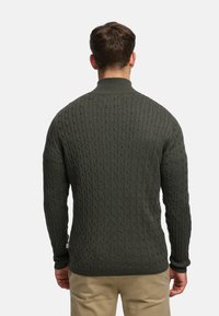 Ciemnozielony sweter z dzianiny o wysokim kołnierzu, z teksturowanym wzorem warkoczowym oraz ściągaczami na mankietach i u dołu. Brak widocznych logo lub zdobień.