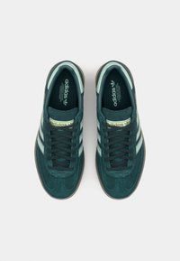 Baskets Adidas, tige en daim vert, lacets foncés, trois bandes latérales bleu clair, semelle en caoutchouc, col rembourré, logo imprimé à l'intérieur.