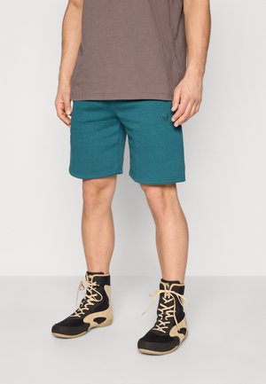 Teal cotton shorts with a logo on the left, paired with black and tan high-top shoes featuring mesh and suede details.