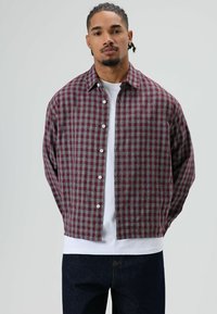 Rotes und graues kariertes Hemd mit durchgehender Knopfleiste, klassischem Kragen und legerer Passform, getragen über einem weißen T-Shirt.