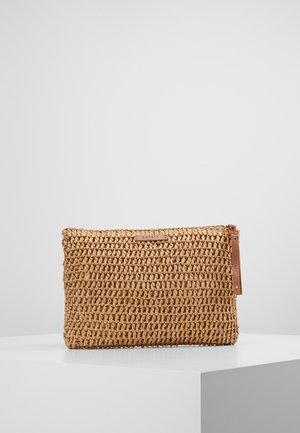 Rechthoekige gevlochten stro clutch met rits en klein leren merketiket, geplaatst op een wit voetstuk tegen een effen achtergrond.