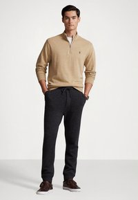 Sweatshirt zíper cinza, calças de fato de treino cinzentas com cordão e calçado castanho. Design simples com texturas suaves e um ajuste descontraído.