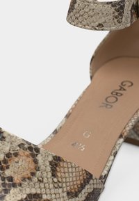 Κλείσιμο σε σανδάλι με μοτίβο φολίδων φιδιού και τακούνι block, που φέρει το όνομα της μάρκας Gabor και την ένδειξη μεγέθους 4 ½ μέσα στην πάτημα.