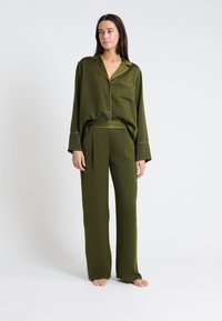 Ensemble de pyjama vert olive en tissu doux ; comprend un haut boutonné à manches longues avec une poche poitrine et un pantalon assorti à coupe ample.