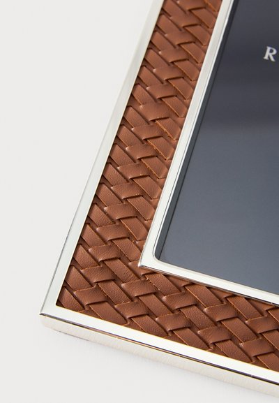 Brązowa pleciona skórzana ramka na zdjęcia z srebrną obwódką. Charakteryzuje się gładkimi krawędziami i płaską powierzchnią do eksponowania zdjęć.