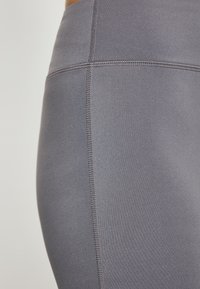 Szürke, rugalmas leggings lapos varratokkal és sima felülettel, a kényelem és a rugalmasság érdekében tervezve. Zsúfolt közeli nézet a oldalvarrat részletéről.