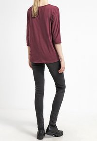 Maroon 3/4-sleeve top with a relaxed fit, paired with black skinny jeans. The outfit features a smooth texture and simple design.