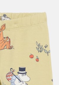 Κίτρινο ύφασμα με καρικατουριστικούς χαρακτήρες, συμπεριλαμβανομένου ενός λευκού ιπποπόταμου με καπέλο  κορδέλα που κρατάει ένα δεμάτι και ενός πορτοκαλί ζώου που κρατάει κόκκινες χάντρες.