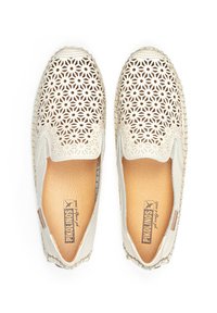 Baskets blanches à enfiler avec un motif en fleurs découpé intricate. Elles présentent une semelle texturée et une doublure intérieure marron avec une étiquette de marque.