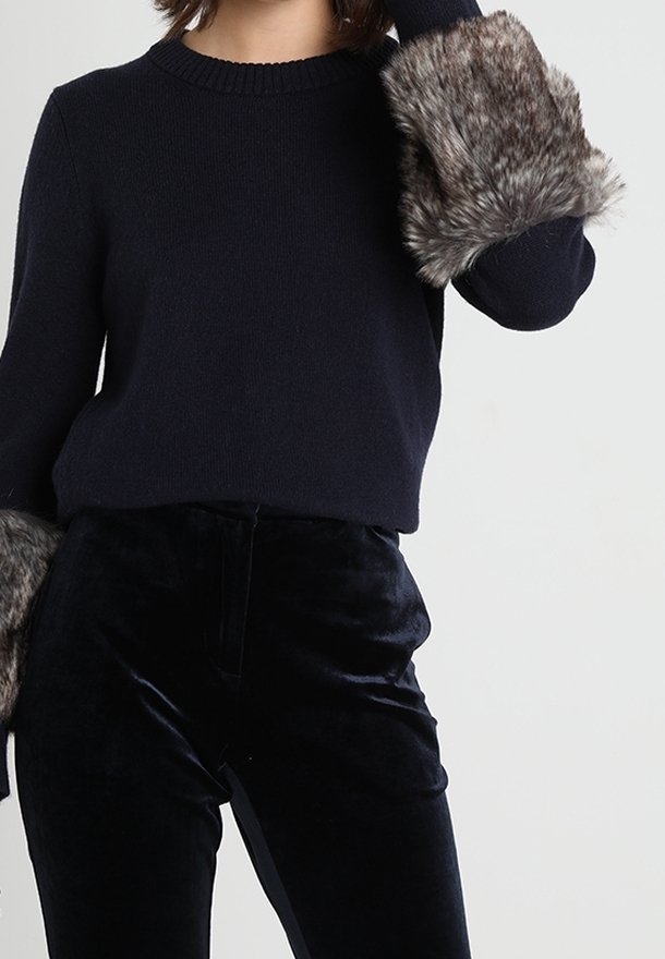 Maglione blu navy con dettagli in pelliccia sintetica grigia a trama ai polsini, abbinato a pantaloni di velluto neri, evidenziando un design elegante e aderente.