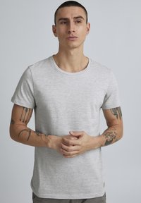 Harmaa ja valkoinen raidallinen lyhythihainen t-paita, jossa on pyöreä kaula-aukko ja teksturoitu pinta, jota käyttää tatuoitu henkilö.