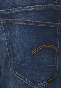 Mörkblå denimjeans med orange sömmar, med en bakficka med en böjd design och en liten svart logotag vid fållen.