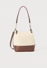 Borsa a tracolla in tela beige con base in pelle marrone, dotata di un manico superiore singolo e tracolla regolabile, accessori in argento e dettagli minimalisti.