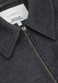 Ciemnoszara kurtka z mieszanki wełny, z szpiczastym kołnierzem, metalowym zamkiem błyskawicznym oraz metką z informacjami o marce i rozmiarze.