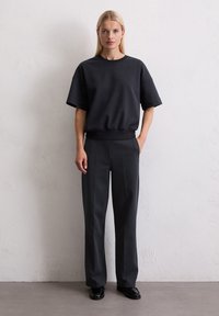 Zwarte oversized sweatshirt met korte mouwen en geribbelde zoom, gecombineerd met hooggezette, op maat gemaakte zwarte broek en glanzende zwarte schoenen.