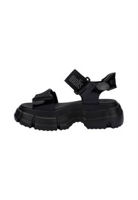 Czarne, masywne sandały z teksturowaną podeszwą, z regulowanymi paskami i błyszczącym wykończeniem. Górna część zawiera oznaczone logo pasek dla dodatkowego detalu.