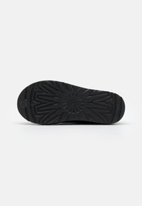 Semelle en caoutchouc noir avec motif de bande de roulement en zigzag et centre texturé circulaire, présentée sur un fond clair uni.