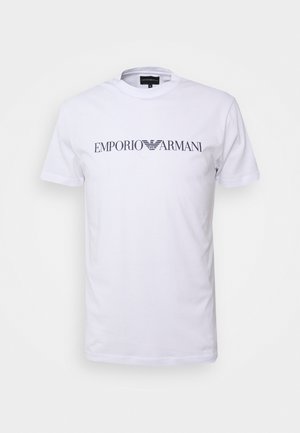 Bela bomba majica iz bombaža s krojem okoli ovratnika in kratkimi rokavi, na prsih pa prikazuje logo "EMPORIO ARMANI" v temno sivi barvi.