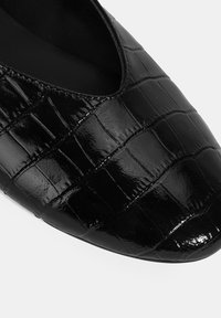 Schwarze Lacklederschuhe mit spitzer Zehe, die eine erhabene Krokodilhautstruktur und ein tiefes V-Ausschnittdesign am Spann aufweisen.