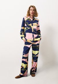 Knoopshirt en wijdvallende broek in kleurrijk abstract patroon. Gemaakt van een soepele stof in marineblauw, roze, geel en groene tinten.