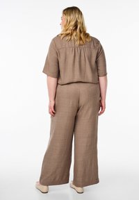 Hnědý lněný dvoudílný outfit s krátkými rukávy a širokými kalhotami, s texturovaným povrchem a volným, uvolněným střihem.