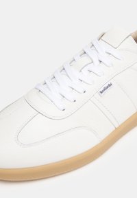 Hvide lædersneakers med tekstureret overdel, rund tå og hvide snørebånd. Har en lys brun gummisål og et diskret logotag.