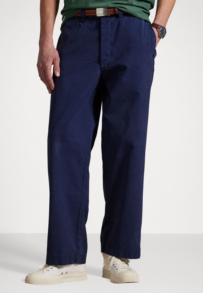 Pantalon en coton bleu marine avec une coupe décontractée, doté de poches latérales et d'une finition légèrement texturée, associé à des baskets beiges.