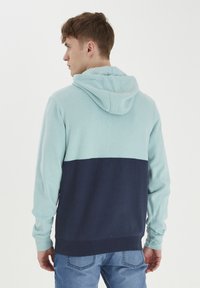 Hoodie s gornjim dijelom u mint zelenoj boji i donjim dijelom u mornarsko plavoj boji. Mekani materijal s dugim rukavima te rebrastim manžetama i rubom.