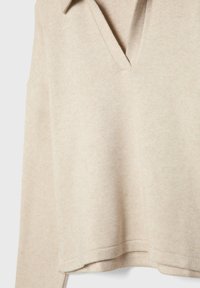 Maglione beige a collo a V con una vestibilità rilassata, maniche lunghe e una consistenza morbida. Presenta una finitura a cucitura sull'orlo e dettagli sul colletto.