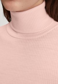 Light pink ribbed turtleneck top with a high collar, featuring a soft texture and fitted design, emphasizing vertical lines and simplicity.