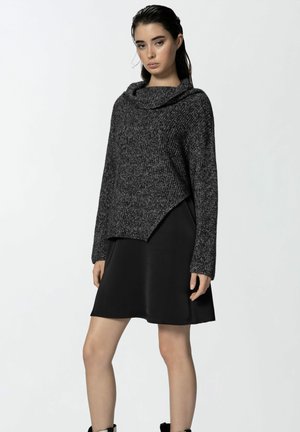 Maglione a maglia in carbone con scollo a dolcevita e orlo asimmetrico, abbinato a un vestito in satin nero. Maniche lunghe con polsini a coste.