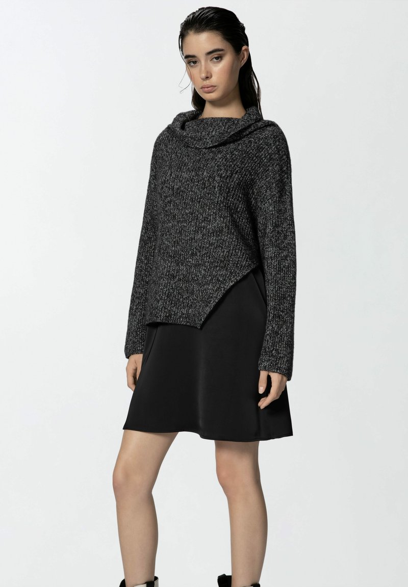 Maglione a maglia in carbone con scollo a dolcevita e orlo asimmetrico, abbinato a un vestito in satin nero. Maniche lunghe con polsini a coste.