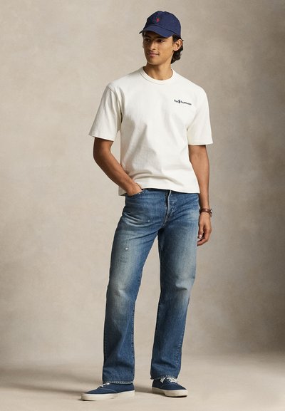 Ανοιχτό μπεζ κοντομάνικο μπλουζάκι, μπλε τζιν με ξεθωριασμένες λεπτομέρειες και σκούφο μπλε ναυτικού χρώματος. Αθλητικά παπούτσια σε μπλε αποχρώσεις συμπληρώνουν το σύνολο.