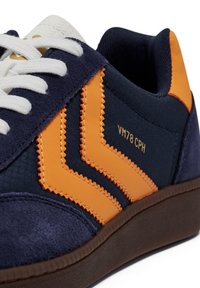 Marina och orange sneakers med detaljer i mocka och tygmaterial, zickzack-sömmar, vita snören och en texturerad brun gummisula.